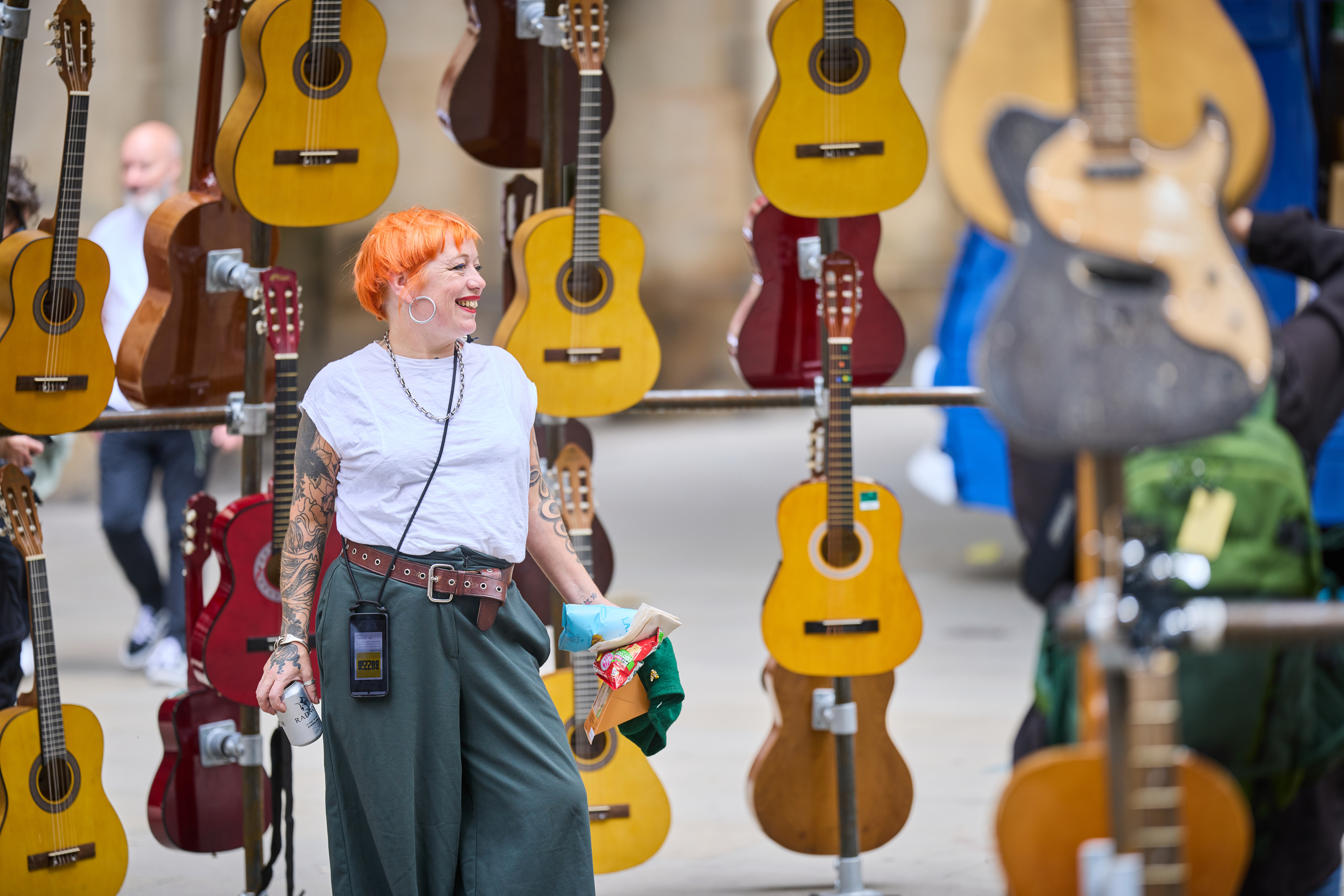 Smiling woman standing on a street with lots of guitar hanging in the air behind her
