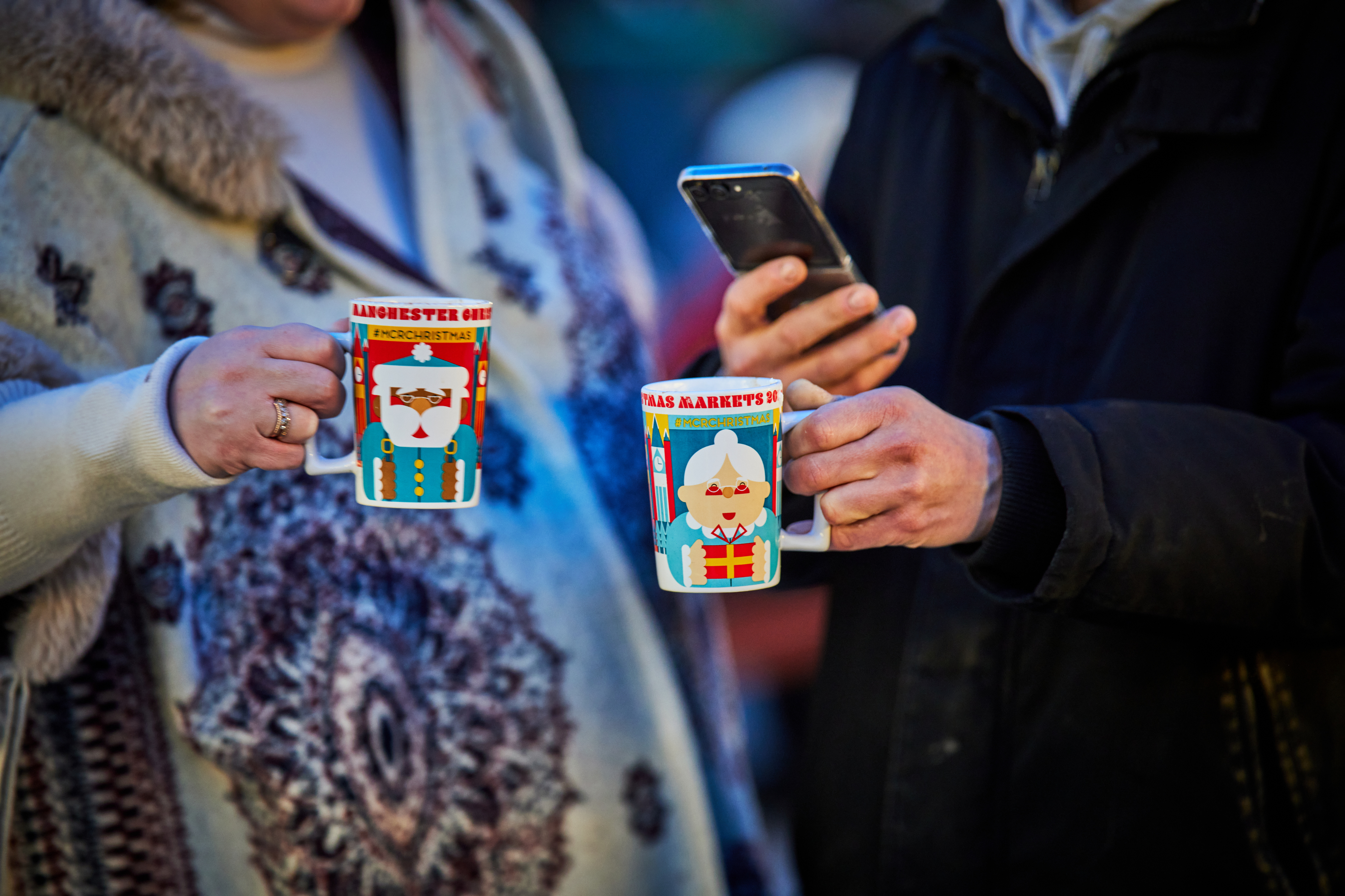 Close-up of two festive Christmas mugs being held in the hands of two people who faces we can't see