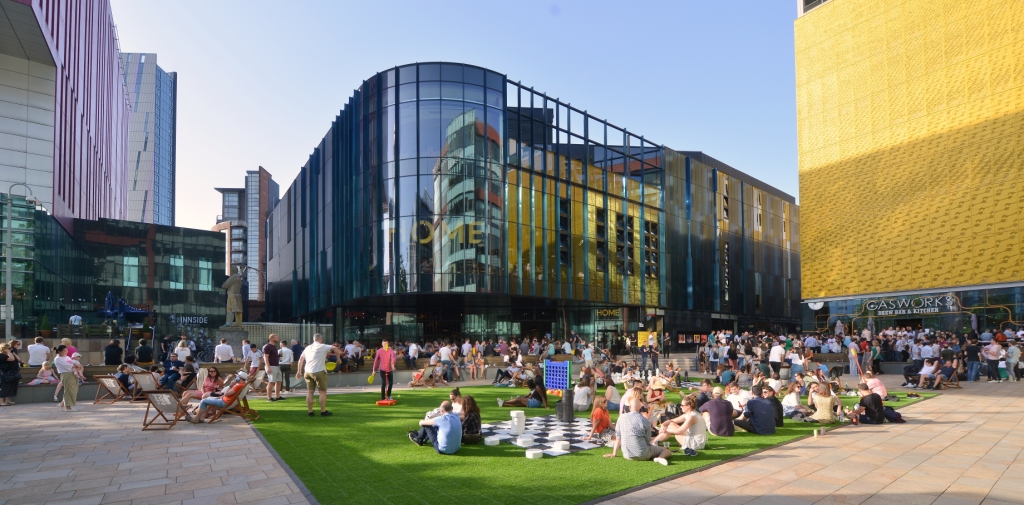 Image of office buildings and a green with people on in front.