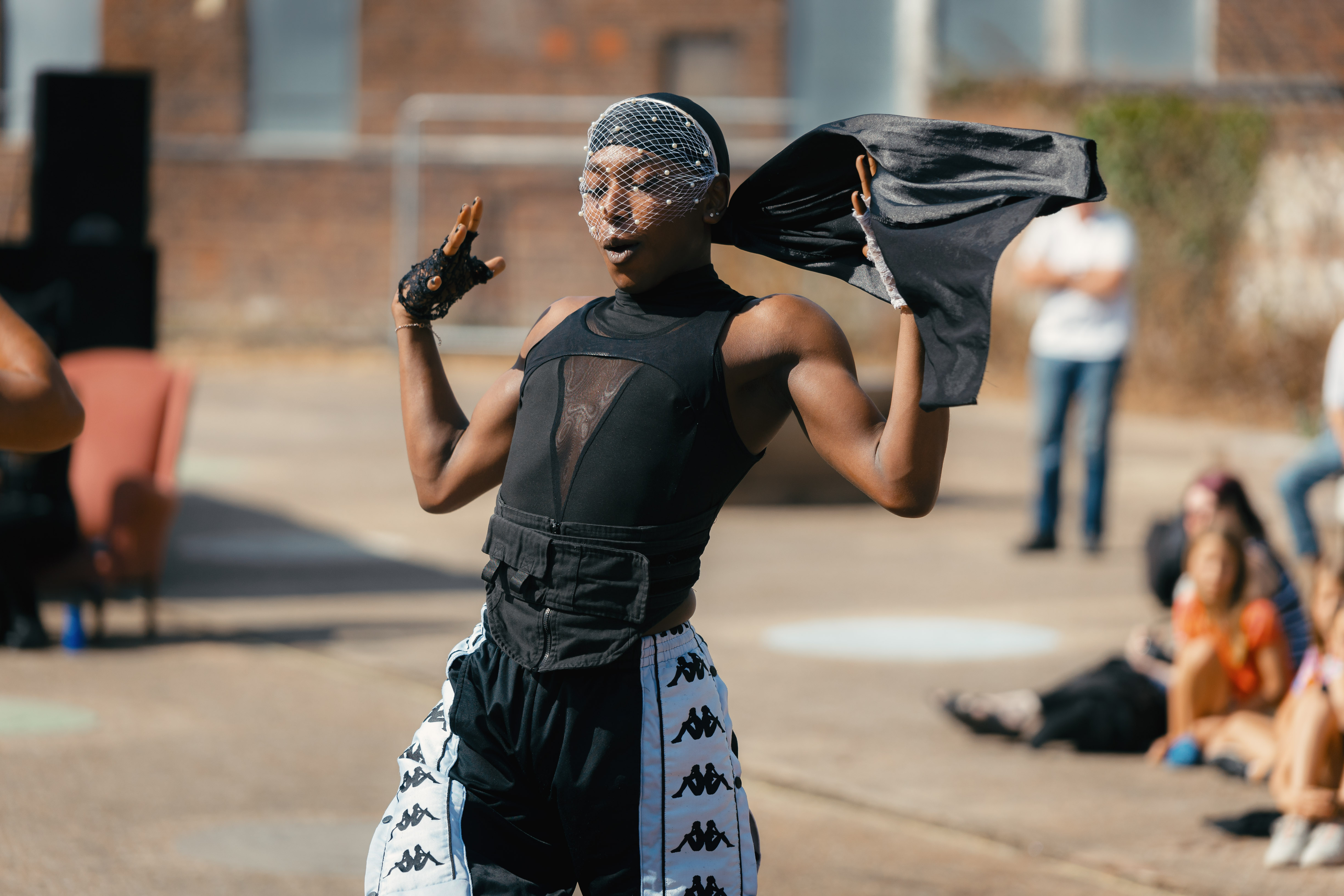 Person wearing a headscarf, holding their hands in the air, dancing in the street