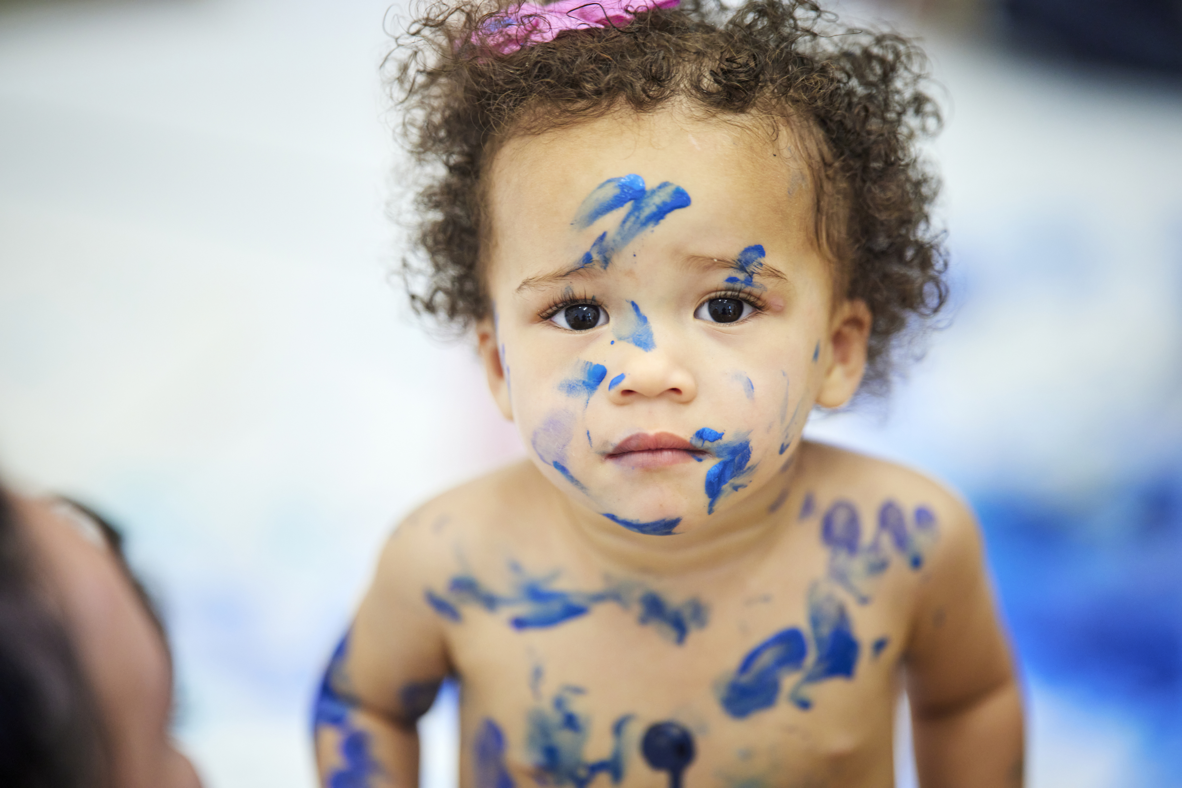 Toddler covered in bright blue paint splashes looks at the camera