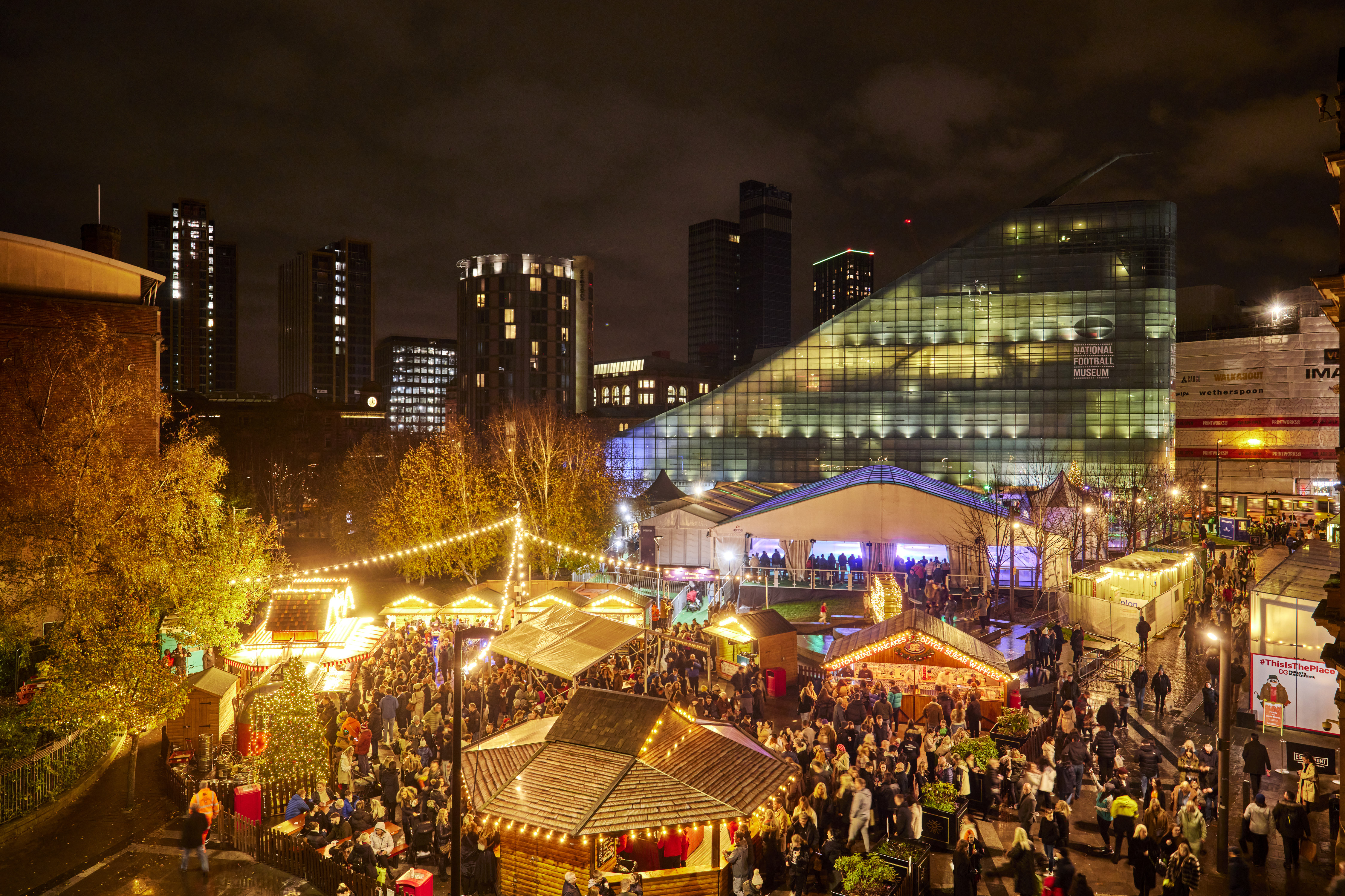Aerial view looking across city scene full of twinkling lights, people and market stalls