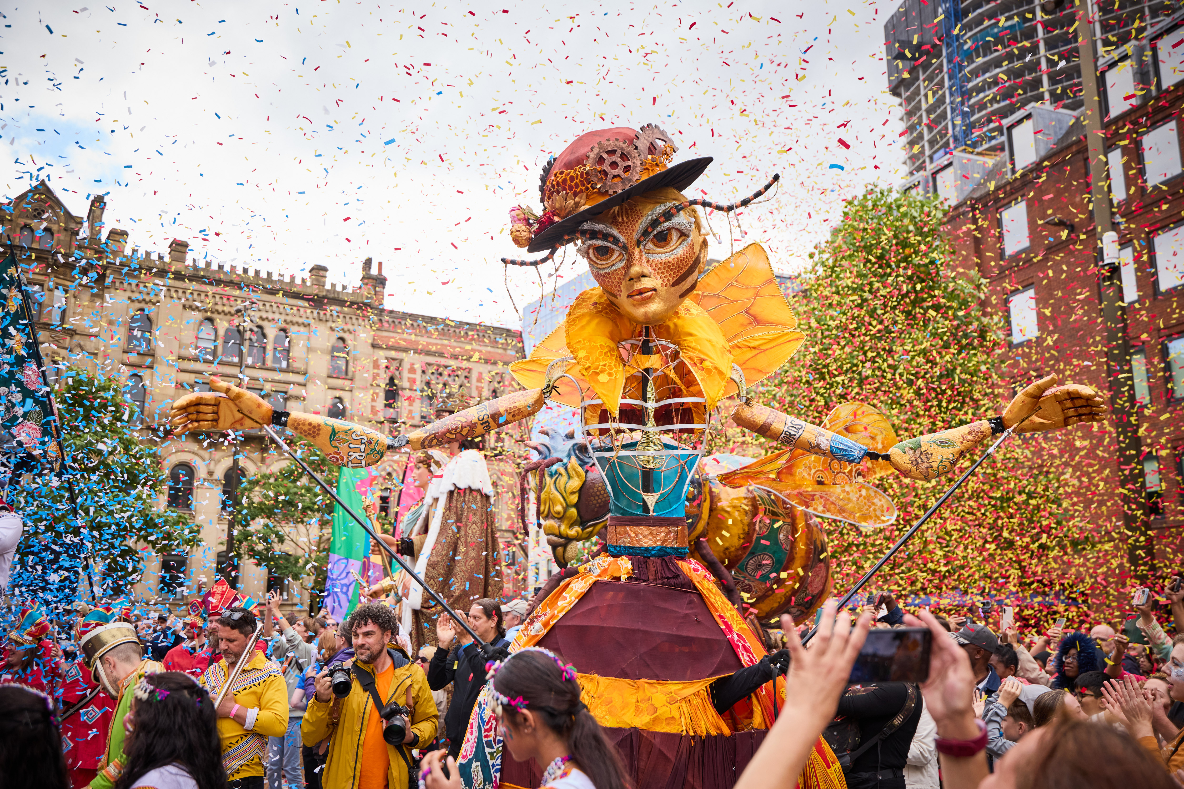 A giant Manchester Queen Bee puppet on Albert Square Manchester with paper confetti raining down on her and crowds all around
