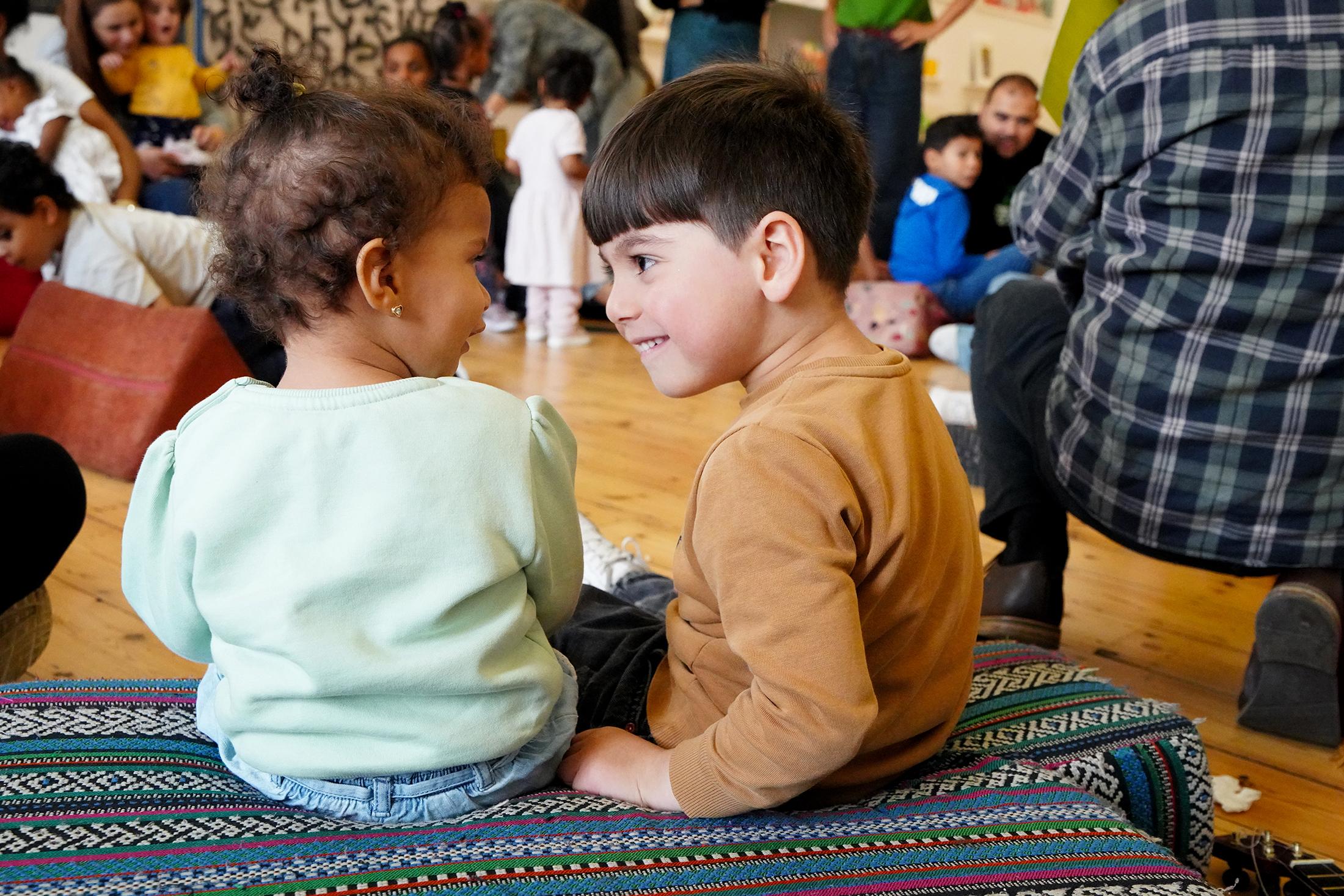 Two small children sitting together looking at each other and smiling