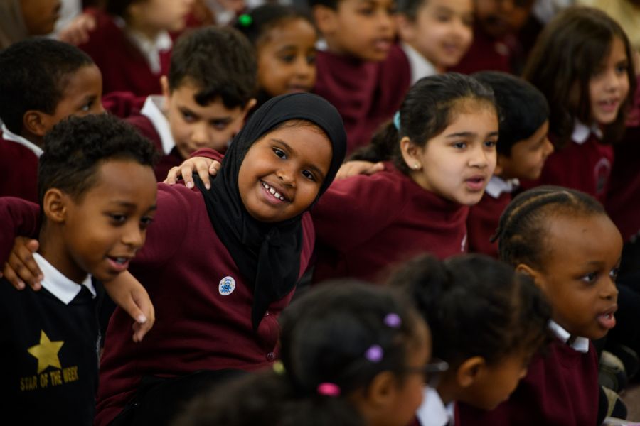An image of a school pupil smiling next to her fellow pupils in an assembly hall