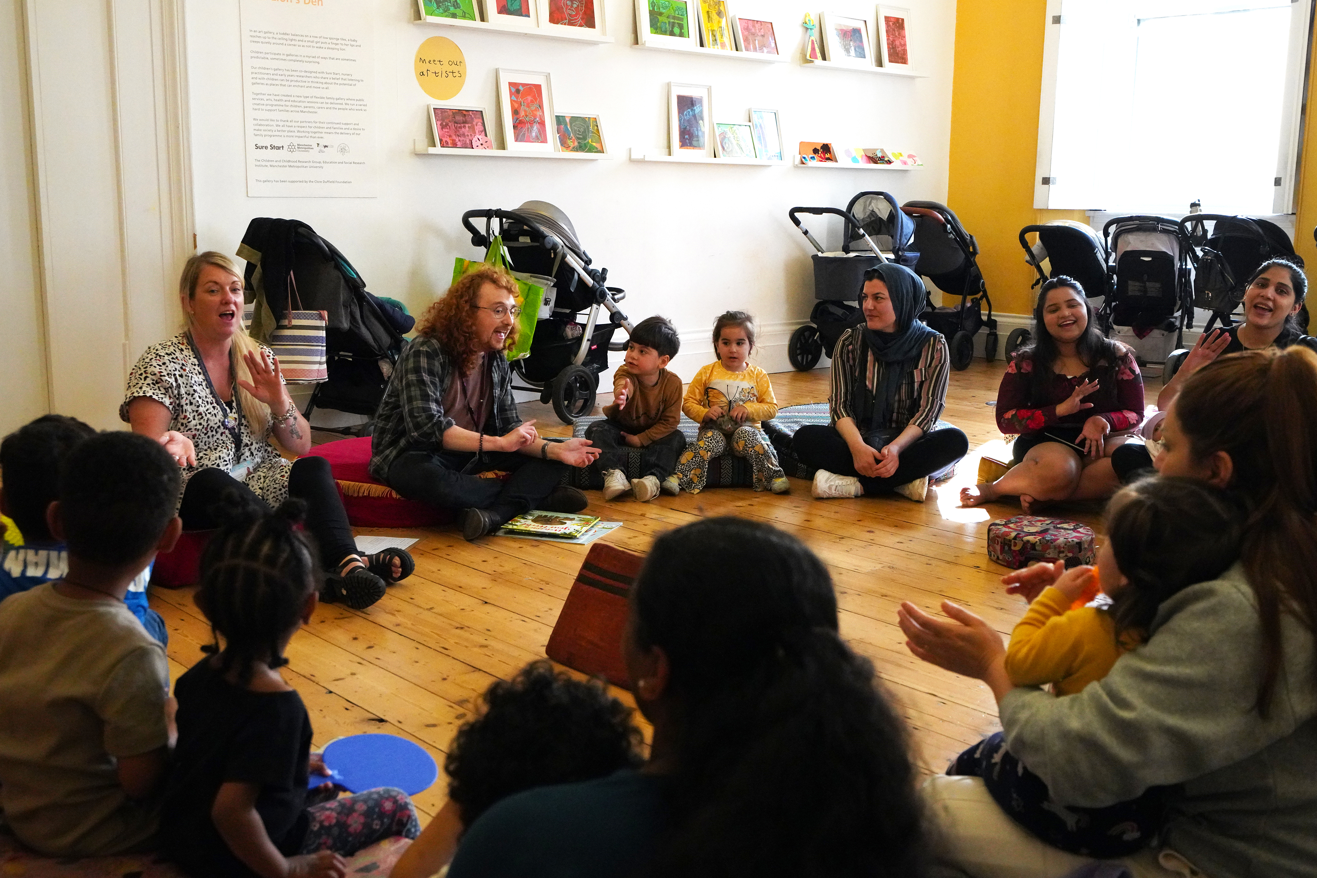 A circle of adults and children sitting together on the floor smiling