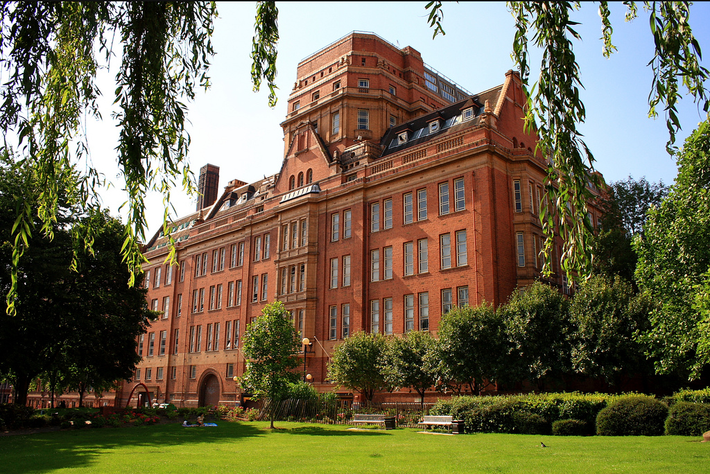 Image of a large red brick building with a green in front