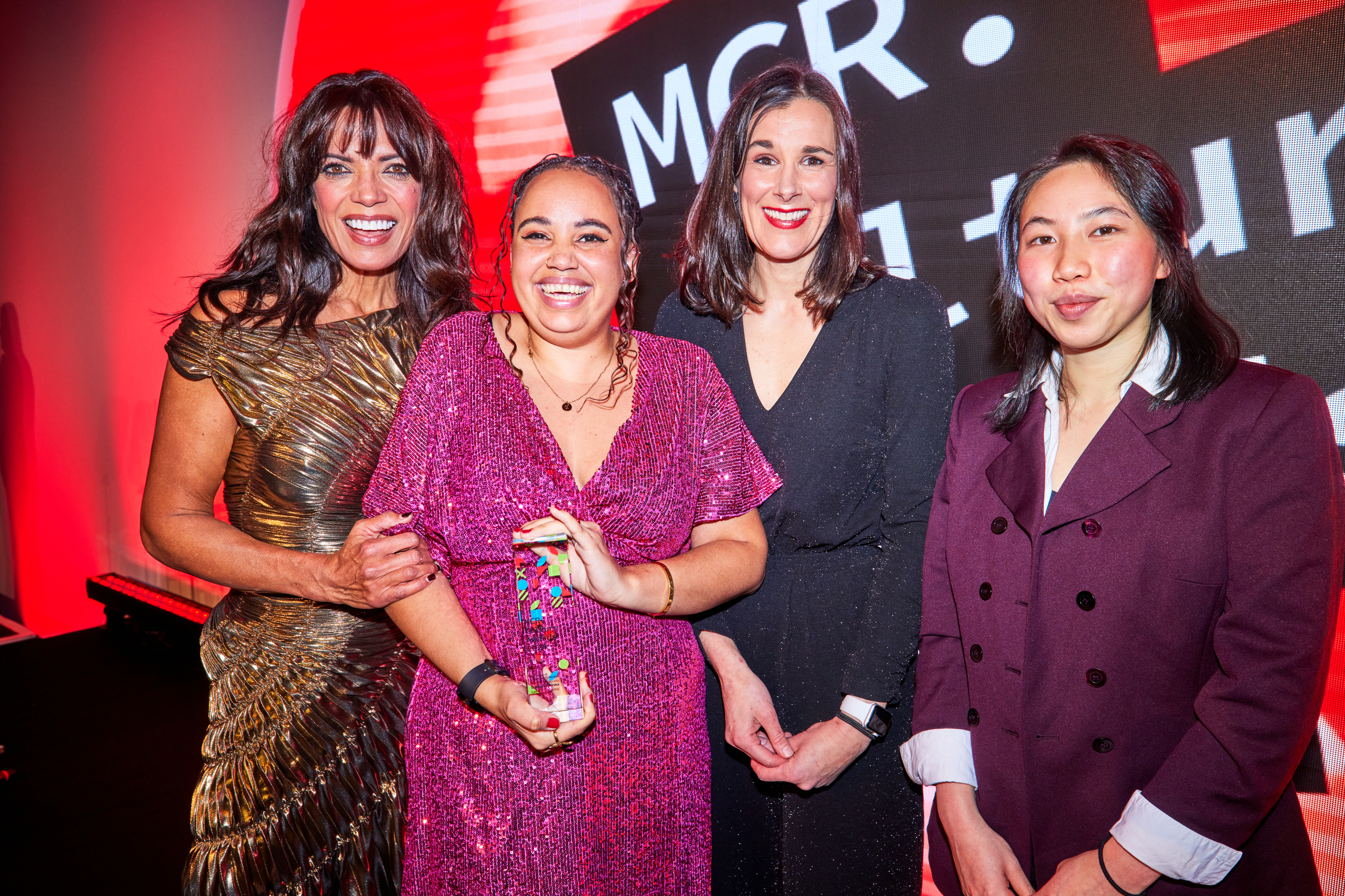 Four people on a stage, smiling at the camera as one person holds up an award