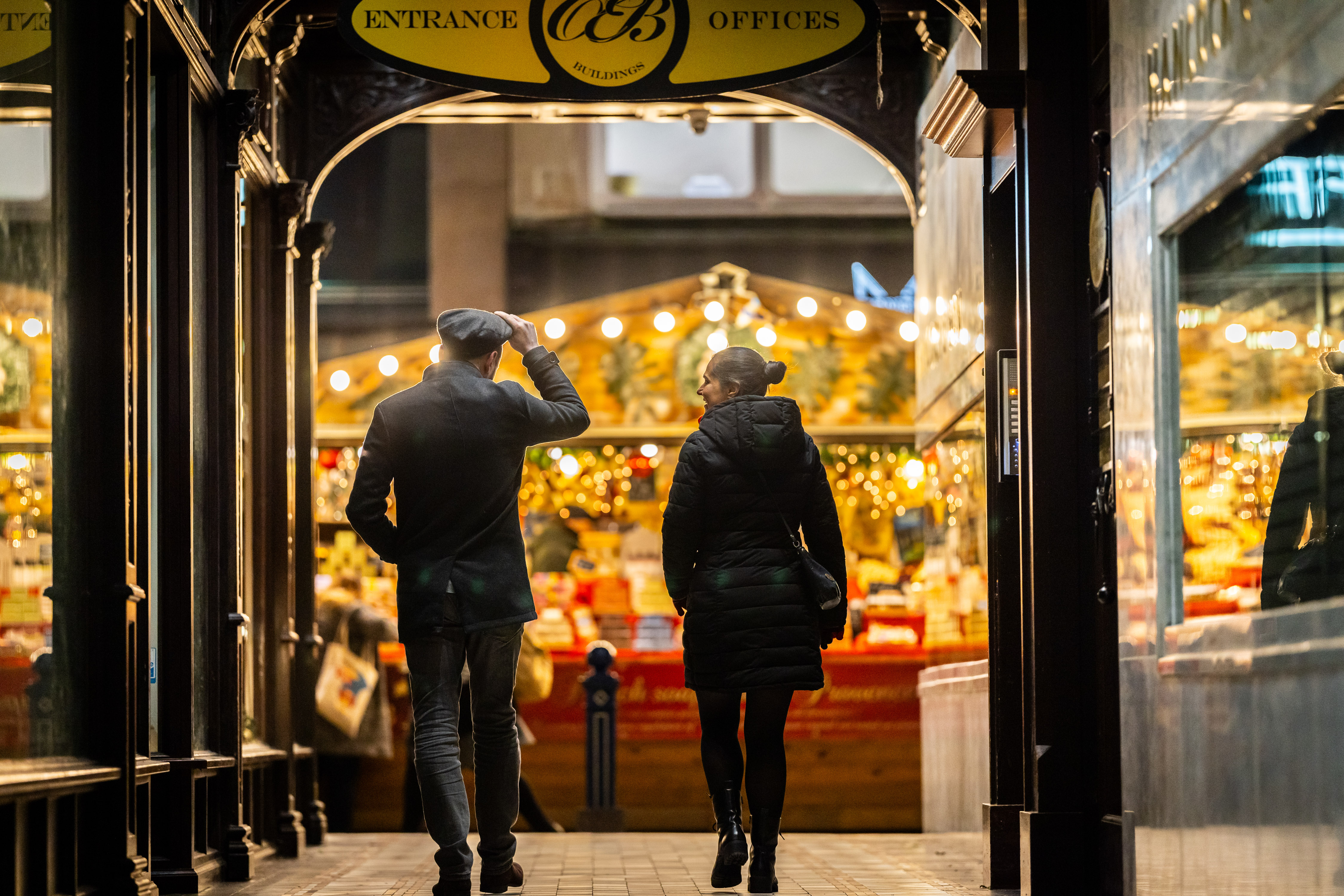 Man and woman walking away from camera towards the bright festive lights of market stalls ahead of them