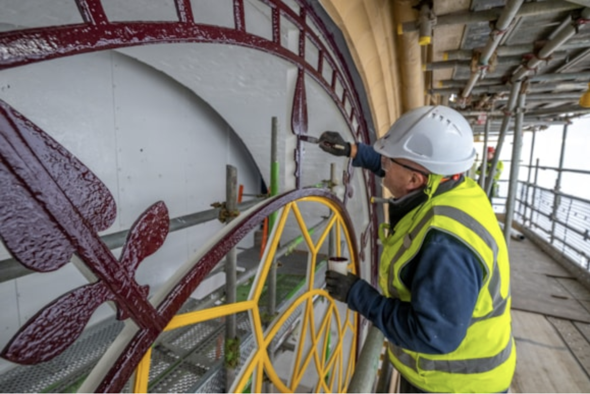 Image of a restoration expert in a hard hat working on the Manchester Town Hall clock face.