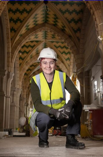 Image shows person in hi-vis vest, hard hat and boots, in a construction setting. 