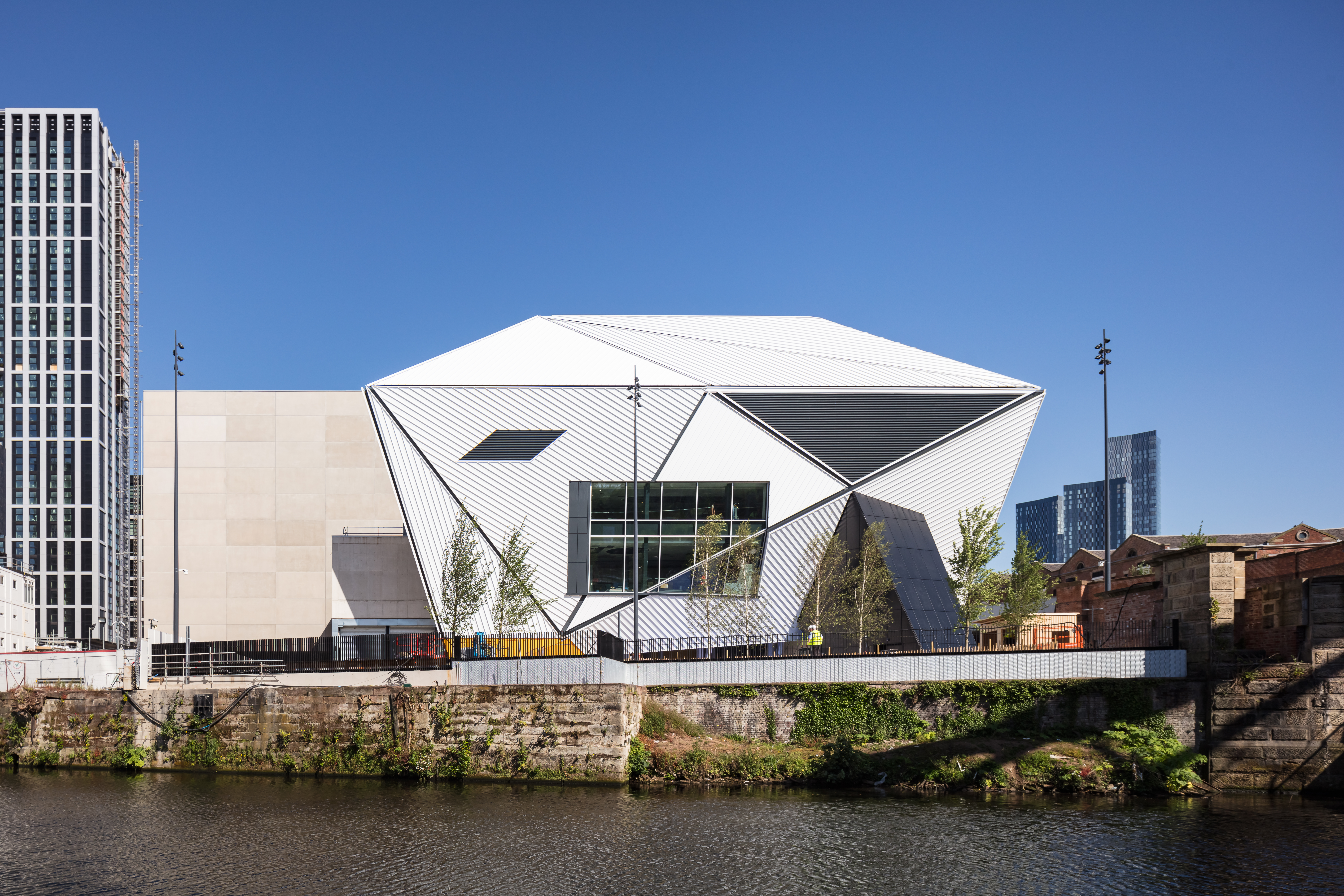 Futuristic building mostly white in colour pictured against a bright blue sky with a rive running in front of it