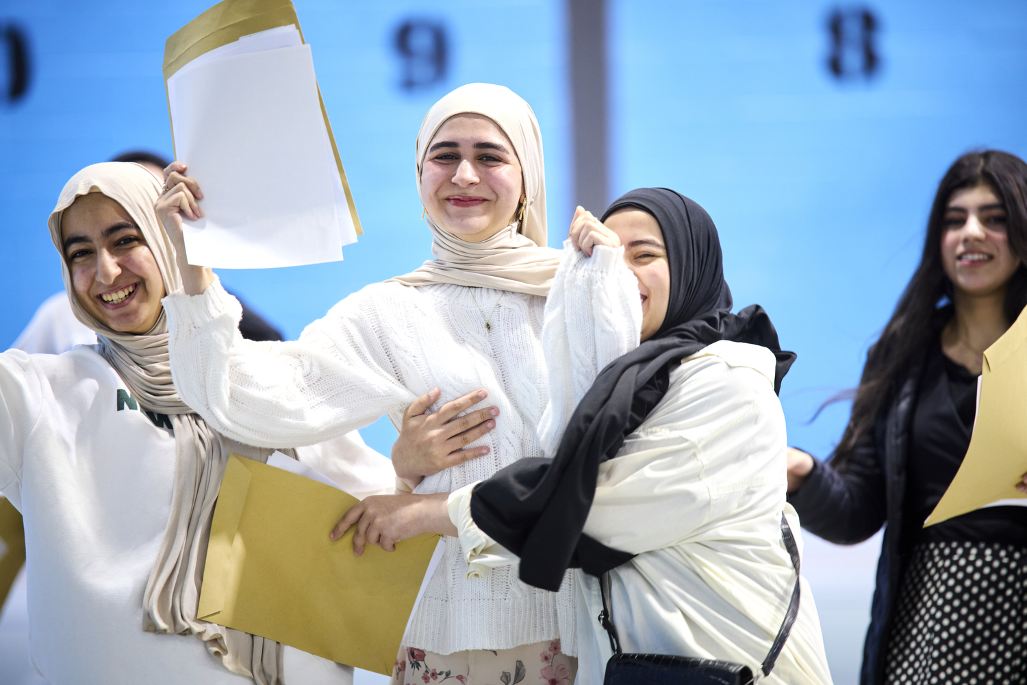 Four young women all laughing holding papers in their hands, one of them being picked up by another