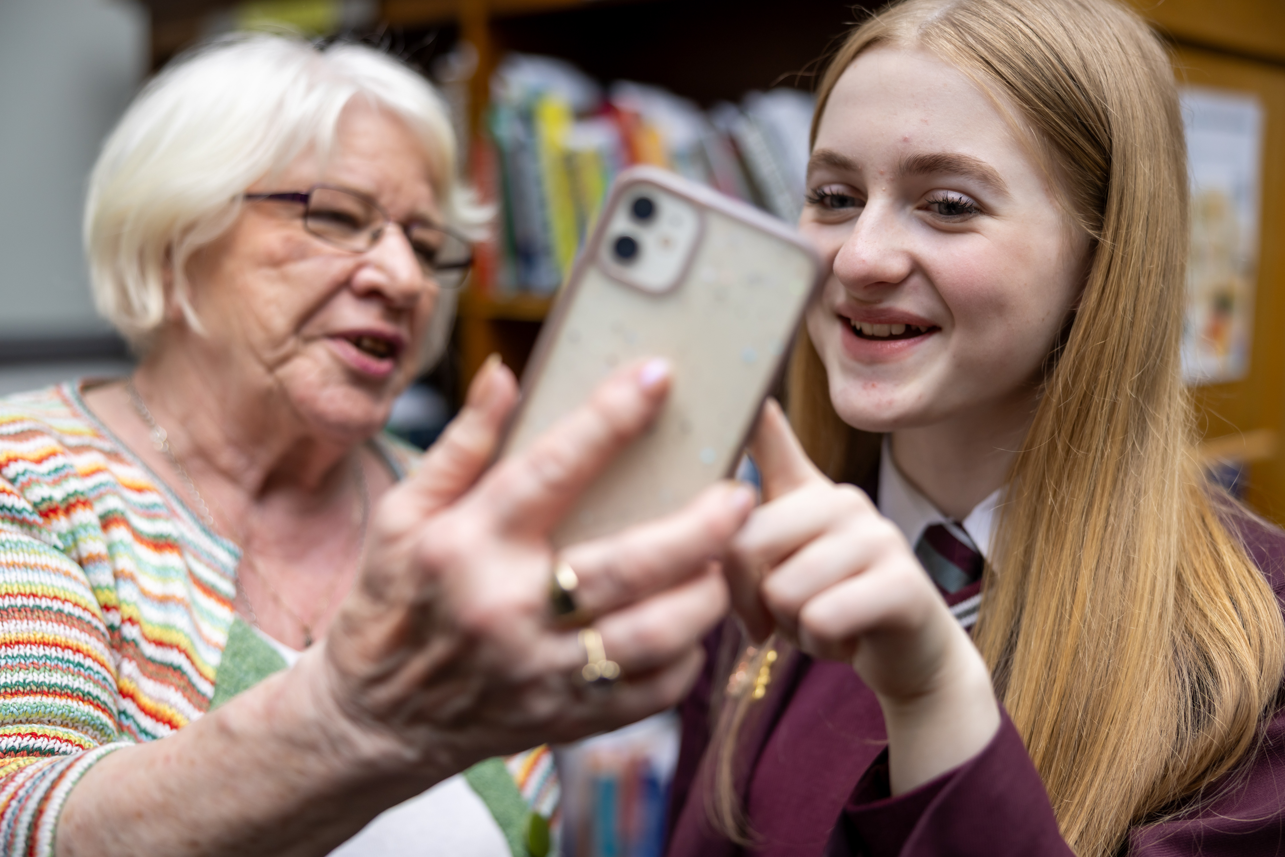 An older woman and teenage girl school pupil both smiling as they look at a mobile phone