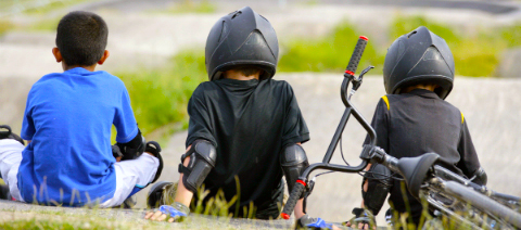 Three kids sitting on a hill with a BMX
