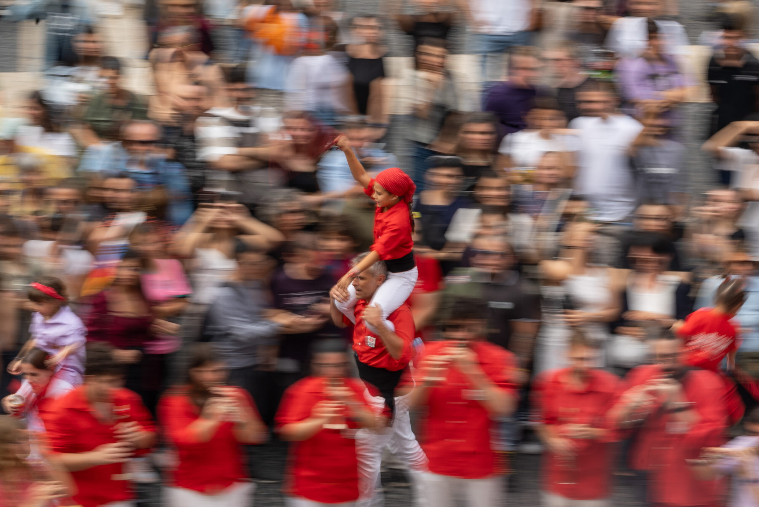 Blurred image of crowds of happy people dressed in red, holding a young person smiling on their shoulders as they move Blurred image of crowds of happy people dressed in red, holding a young person smiling on their shoulders as they move