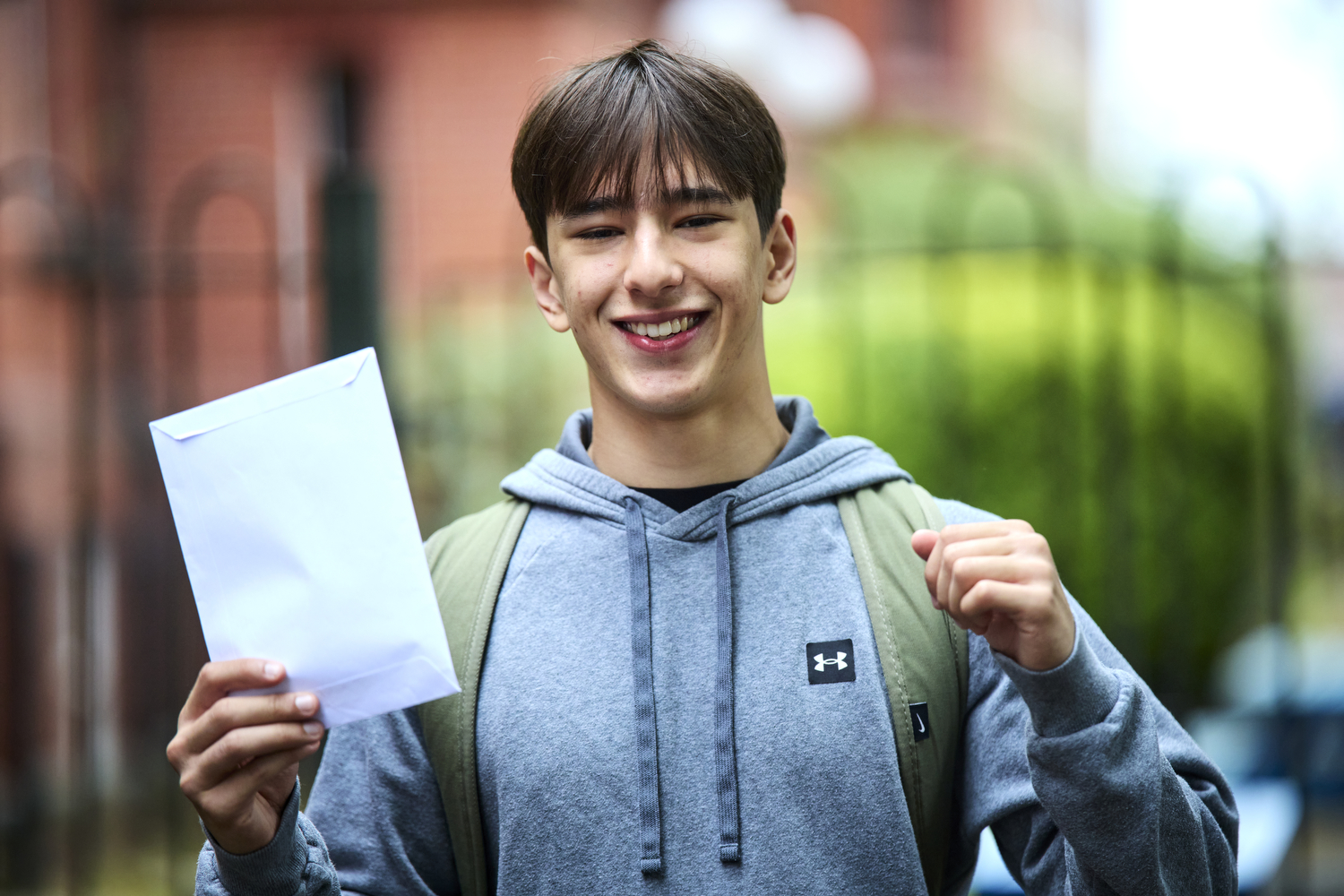 Teenage boy smiling, both arms in the air holding an envelope