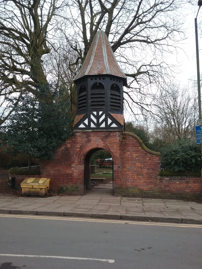 Image of the Lych Gate in Chorlton, a red brick arch with a spire.