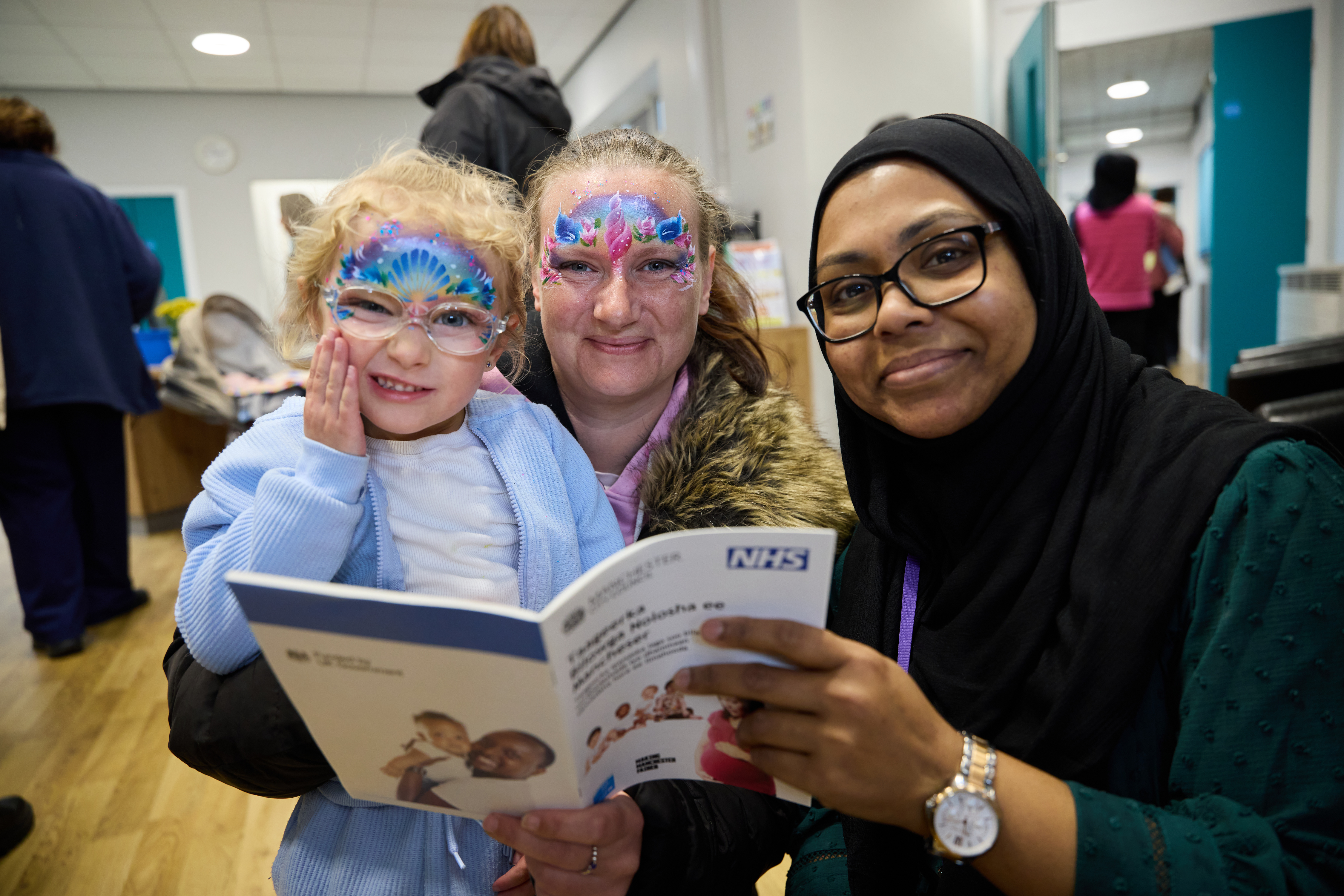 A small child sits with two adults who are all together looking at a booklet 