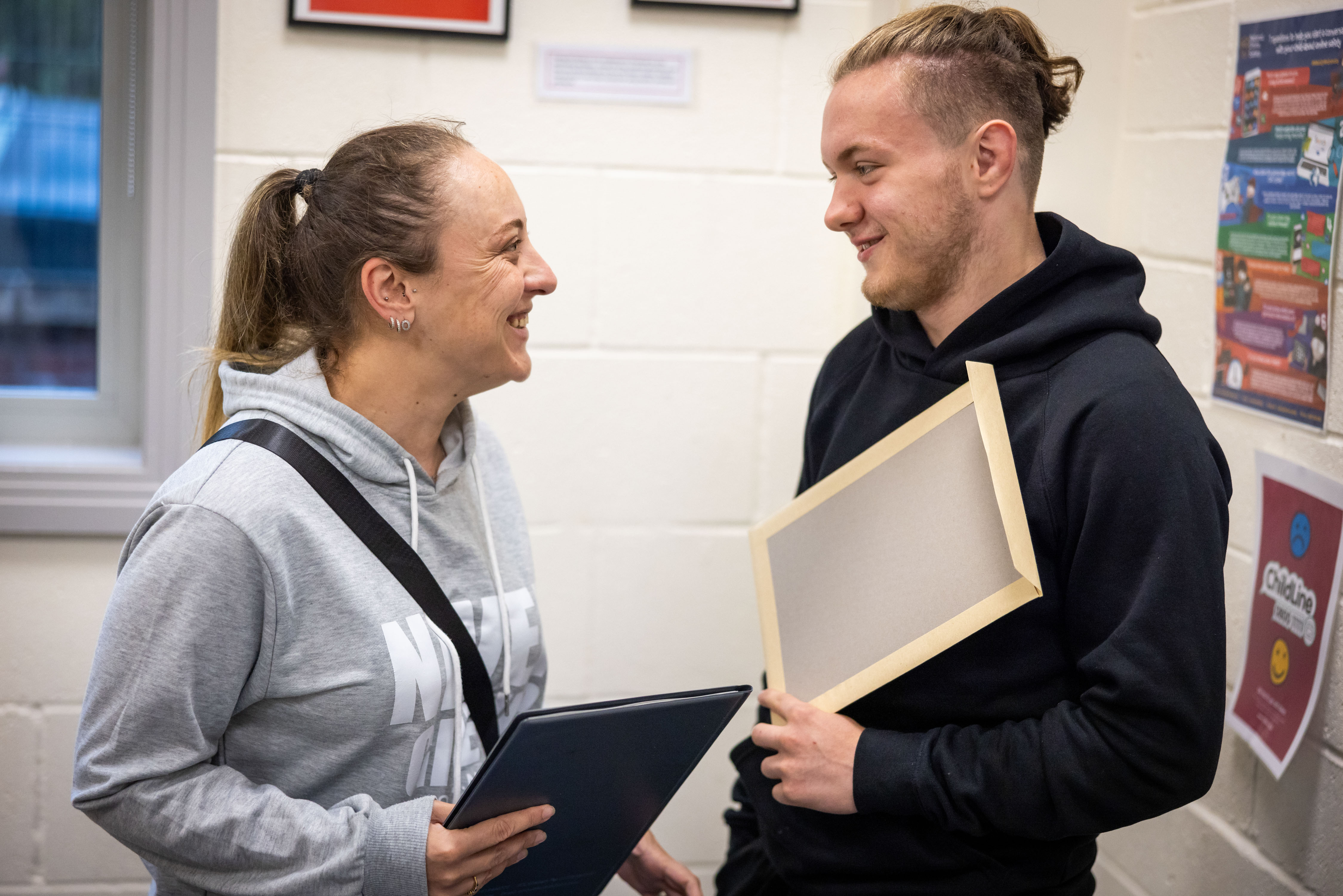 Woman and a teenage boy holding an envelope look at each other smiling Woman and a teenage boy holding an envelope look at each other smiling
