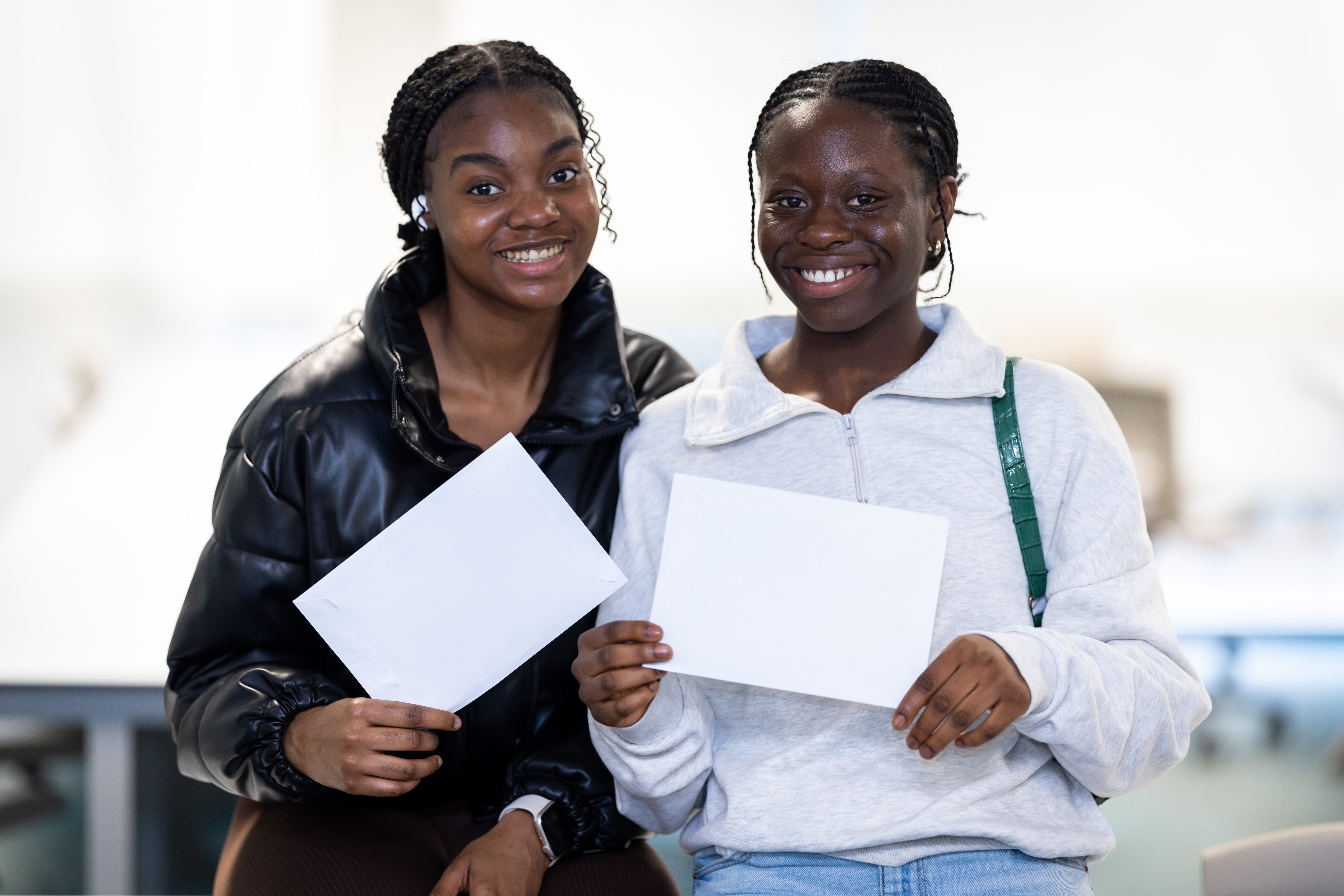 Two teenage girls looking at camera smiling as they hold up envelopes Two teenage girls looking at camera smiling as they hold up envelopes