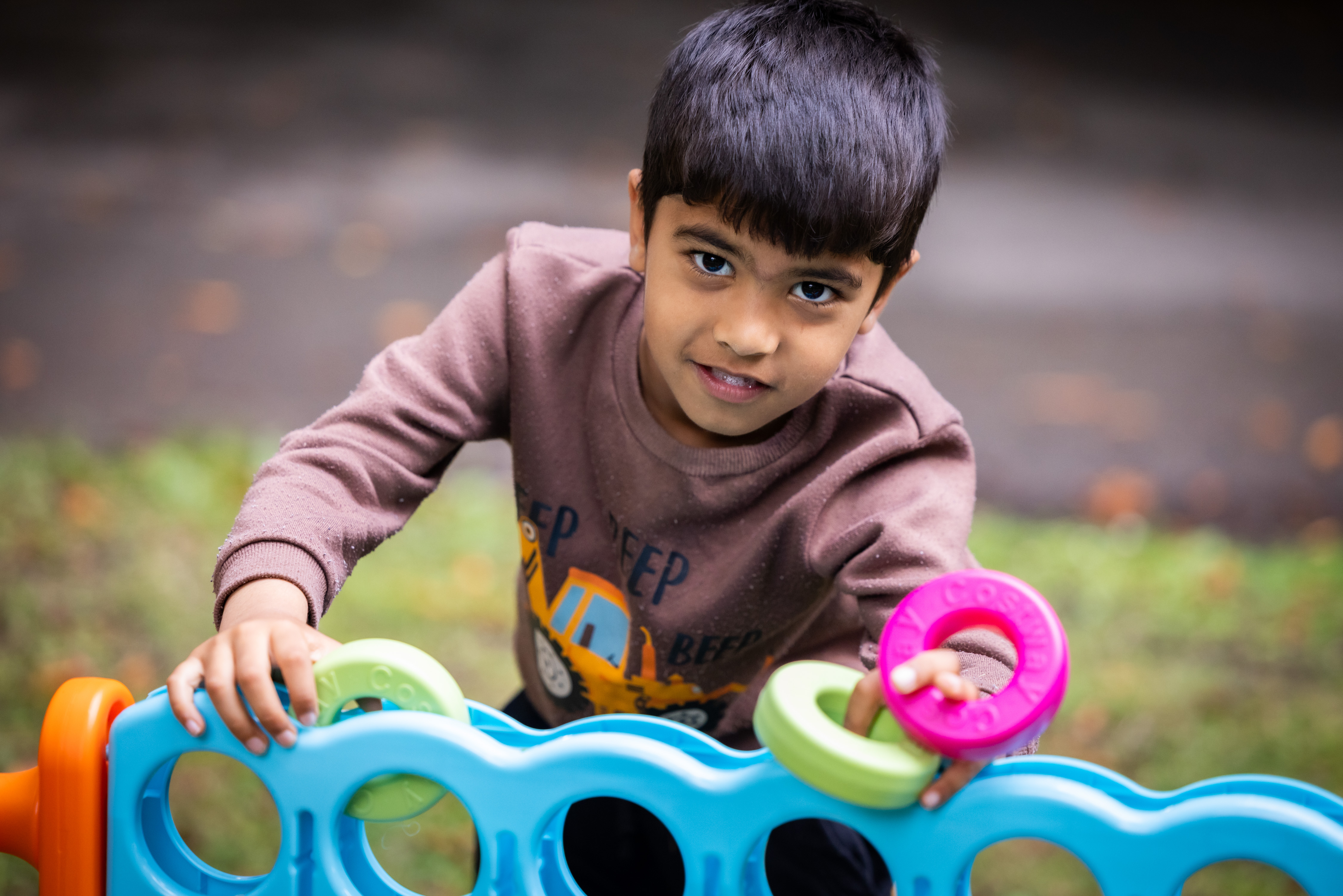A young boy outside in a grassy space smiles at the camera as he holds a coloured ring, part of a giant outdoor game