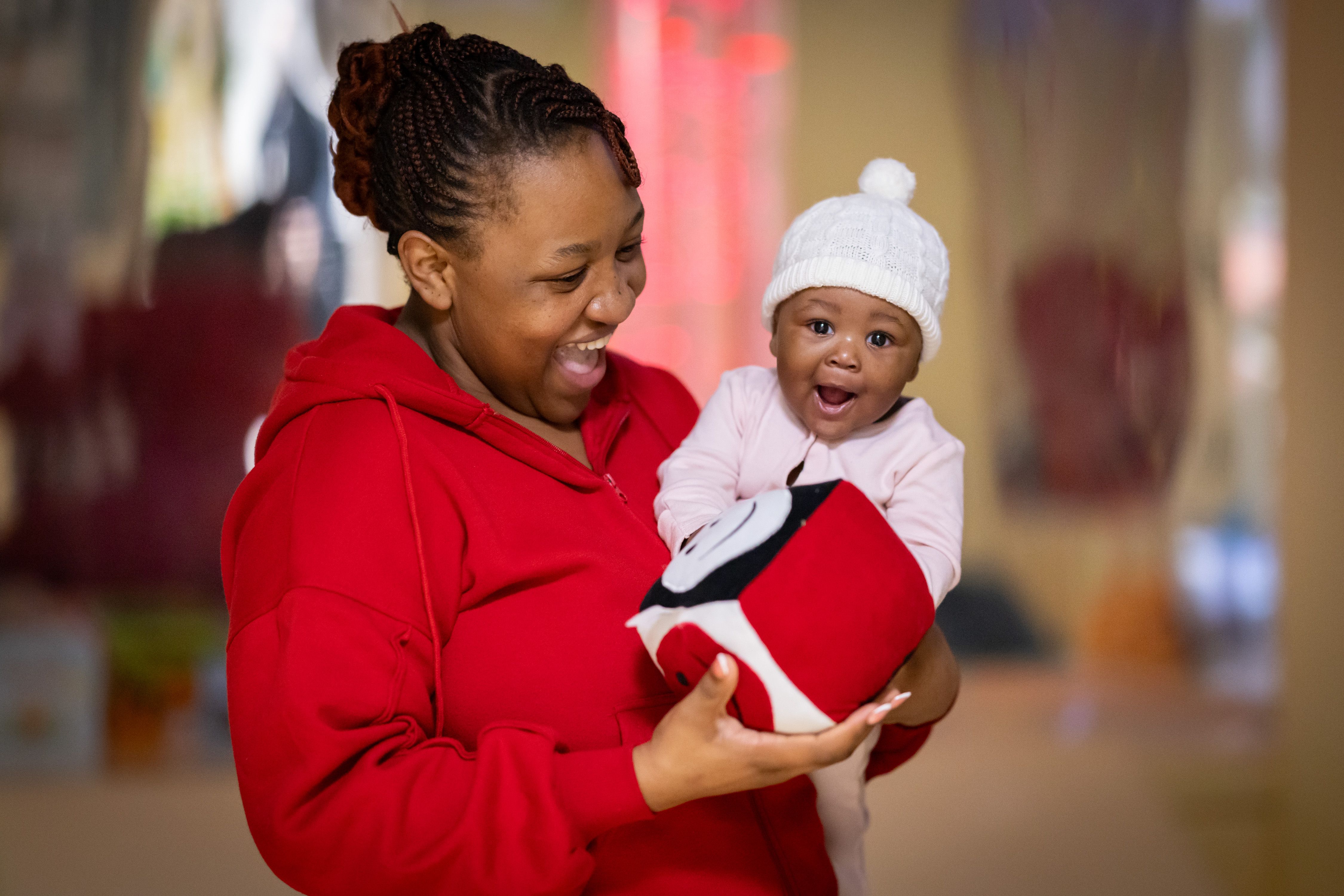 Mother holding a baby in one arm and a soft toy cube in the other mum smiling at her baby and baby smiling at the camera