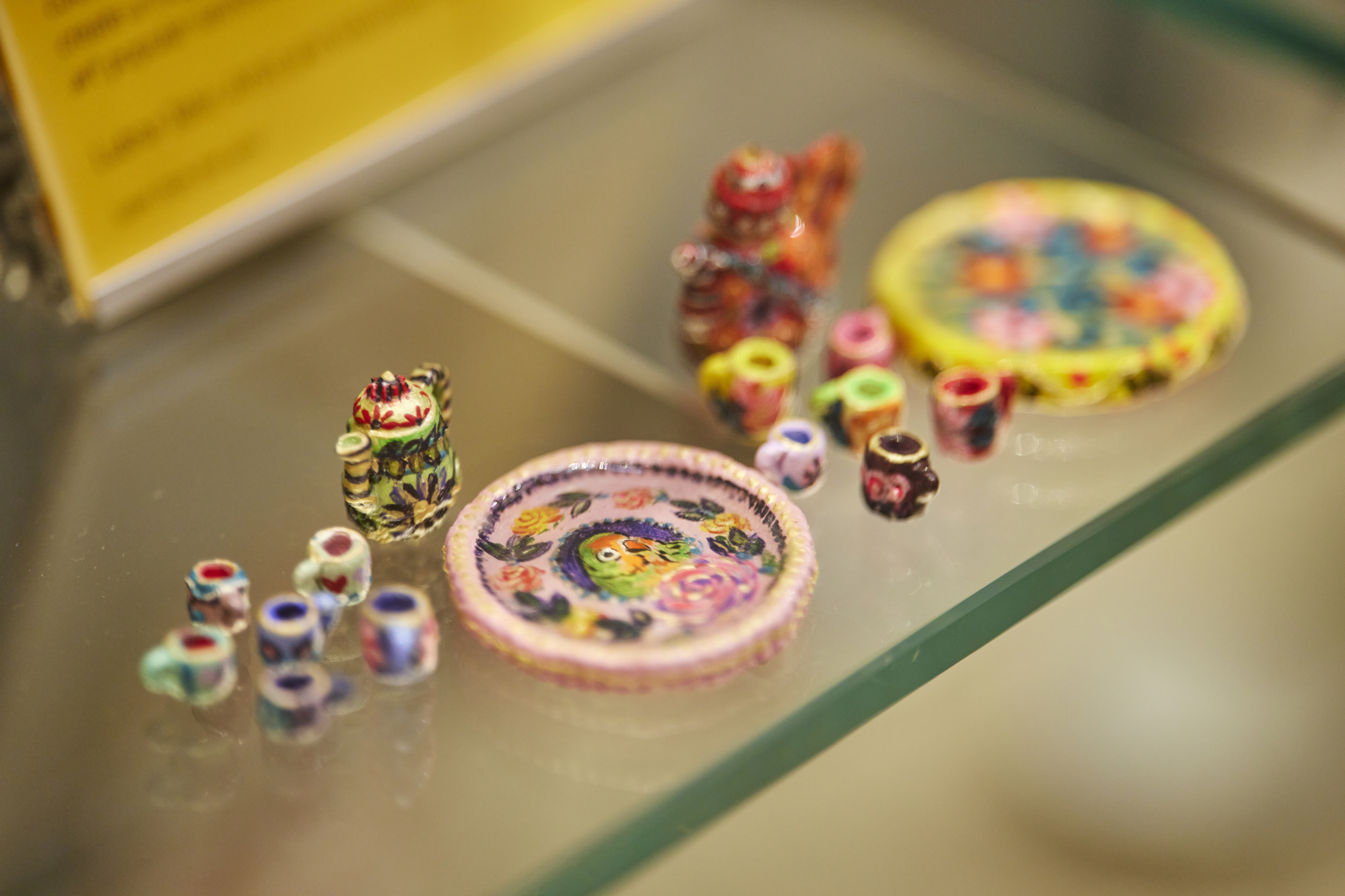 A brightly painted miniature tea service with cups, teapots and plates, sitting on a glass shelf.
