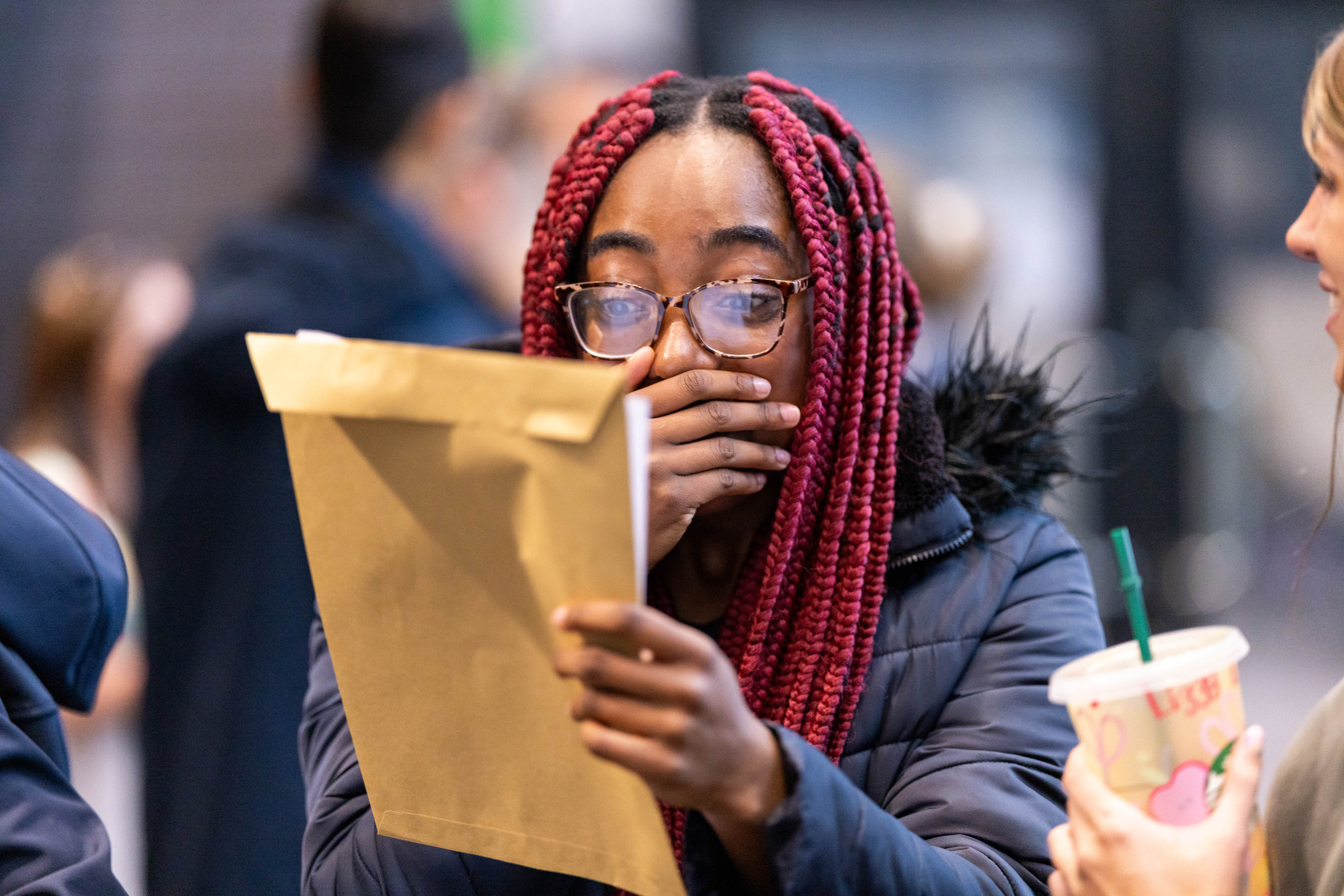 Teenager clasping her hands over her mouth as she looks at a big envelope in her hands Teenager clasping her hands over her mouth as she looks at a big envelope in her hands