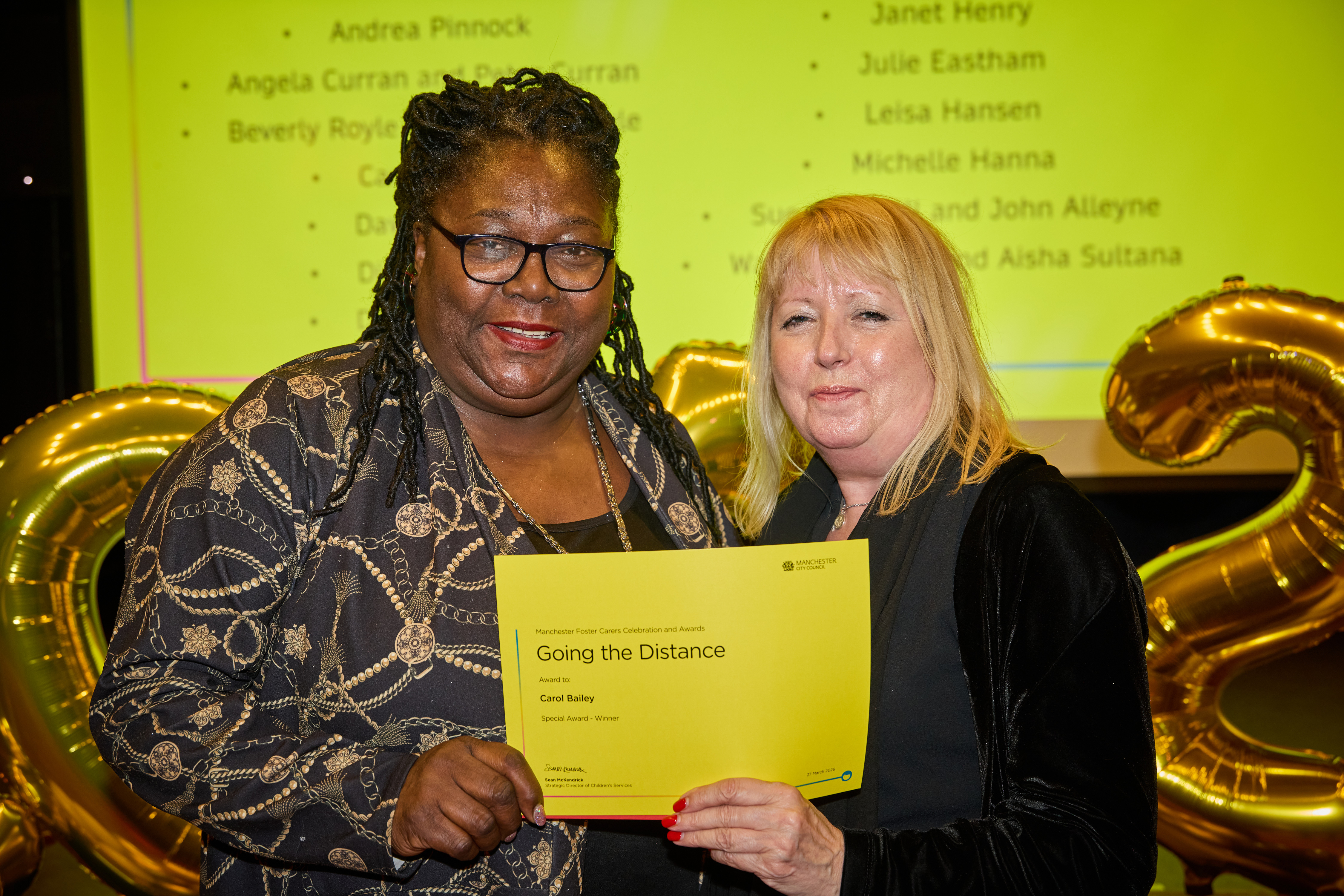 Two women stand together holding up a certificate between them.  One of the women is Councillor Julie Reid and the other is a Manchester foster careruncill
